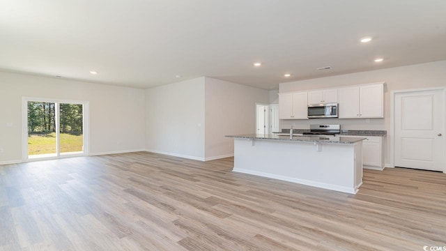 kitchen featuring light stone counters, appliances with stainless steel finishes, a center island with sink, white cabinets, and light wood-type flooring