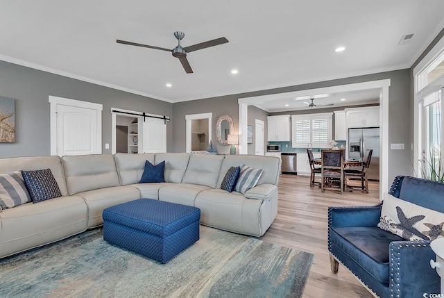 living room featuring light hardwood / wood-style flooring, a barn door, a healthy amount of sunlight, and ceiling fan