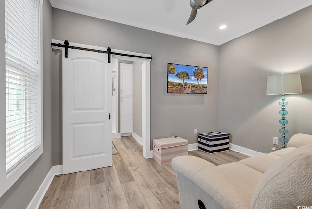 living area with ornamental molding, light hardwood / wood-style flooring, a barn door, and ceiling fan