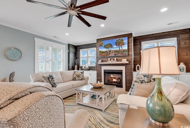 living room featuring ceiling fan, wooden walls, and a large fireplace