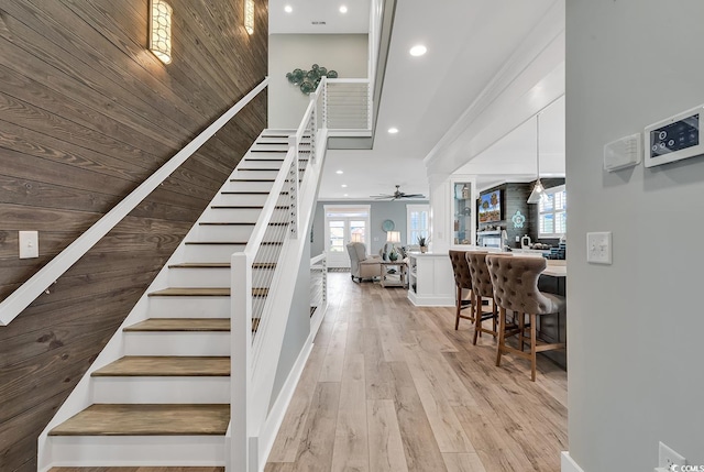 stairs with light hardwood / wood-style floors, a towering ceiling, and ceiling fan