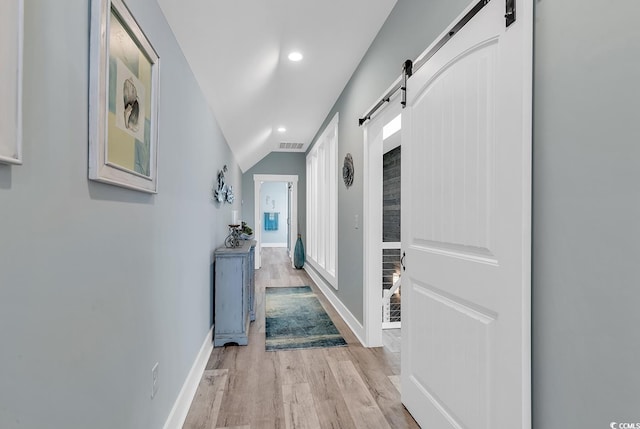 corridor with light wood-type flooring, lofted ceiling, and a barn door