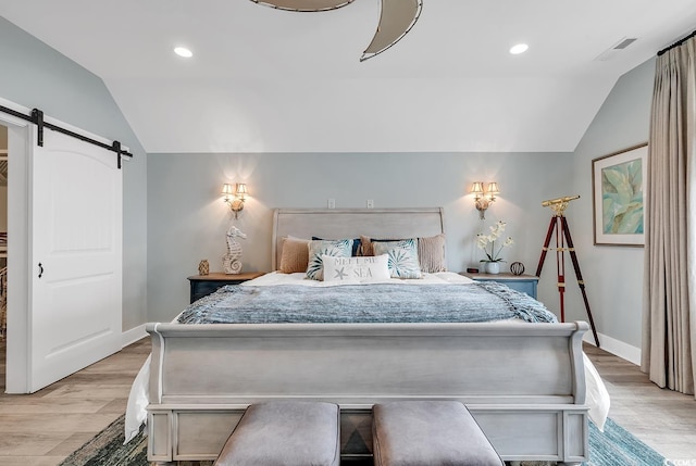 bedroom featuring vaulted ceiling, light hardwood / wood-style floors, and a barn door