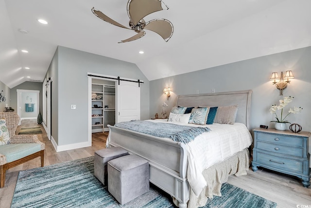 bedroom featuring a spacious closet, a closet, light hardwood / wood-style floors, a barn door, and ceiling fan