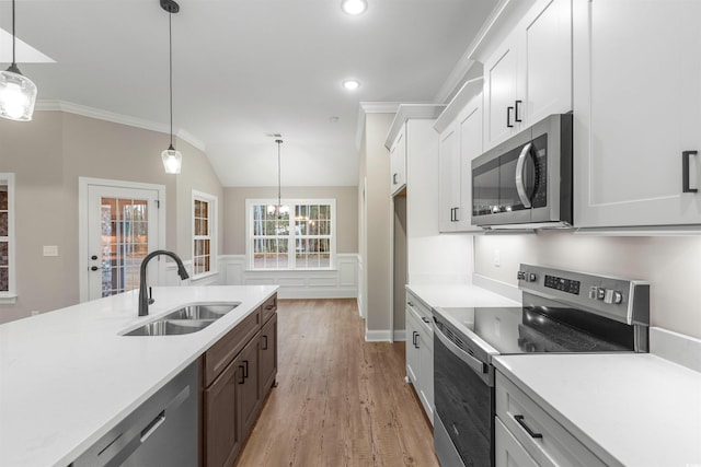 kitchen featuring light countertops, light wood-style flooring, wainscoting, stainless steel appliances, and a sink