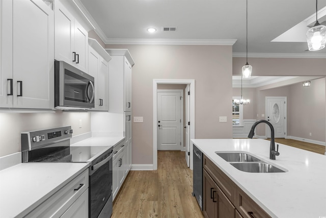 kitchen featuring decorative light fixtures, ornamental molding, stainless steel appliances, white cabinetry, and a sink