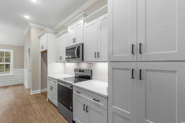 kitchen with light countertops, wainscoting, stainless steel appliances, light wood-style floors, and white cabinetry