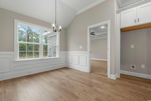 unfurnished dining area featuring ornamental molding, light wood-style floors, an inviting chandelier, wainscoting, and vaulted ceiling