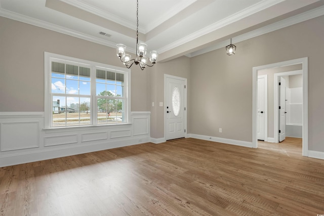 interior space with a raised ceiling, light wood-style floors, an inviting chandelier, and ornamental molding