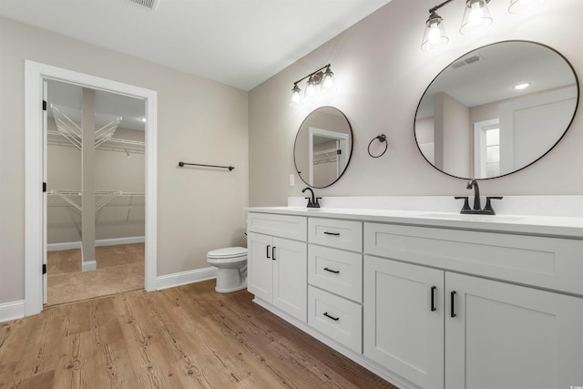 bathroom with double vanity, toilet, wood finished floors, and a sink