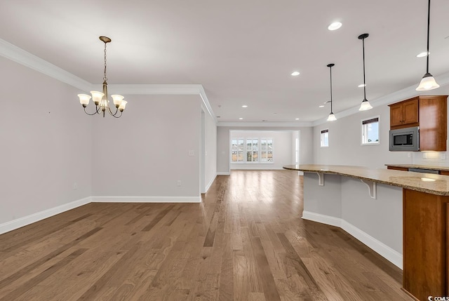 kitchen with a breakfast bar, stainless steel microwave, crown molding, decorative light fixtures, and wood-type flooring