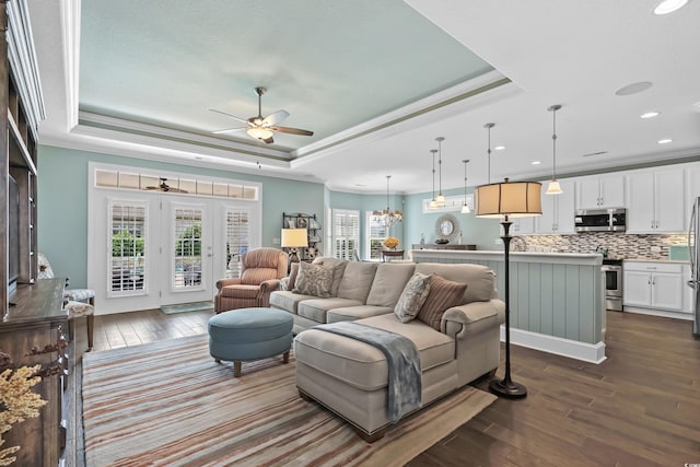 living room with plenty of natural light, ceiling fan with notable chandelier, dark hardwood / wood-style floors, and a tray ceiling