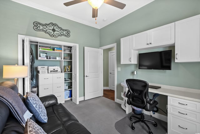 home office with dark carpet, ceiling fan, built in desk, and ornamental molding