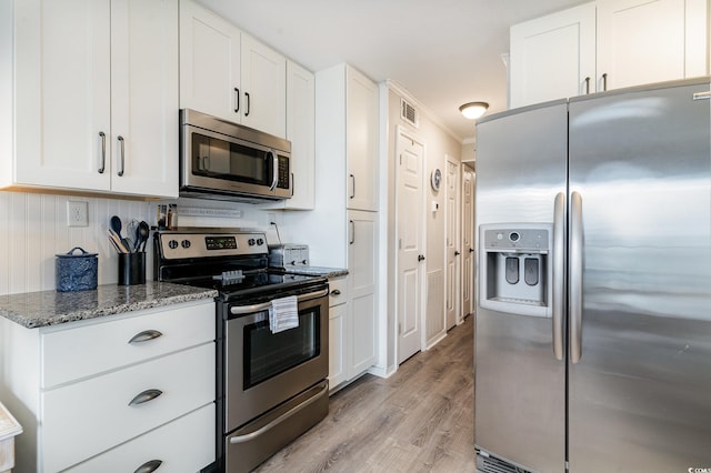 kitchen with white cabinets, stainless steel appliances, light hardwood / wood-style floors, and dark stone counters