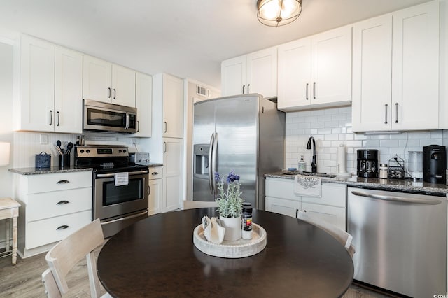 kitchen with hardwood / wood-style floors, backsplash, white cabinetry, dark stone counters, and stainless steel appliances