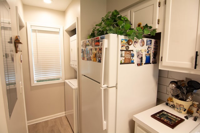 kitchen featuring white fridge, white cabinetry, stacked washer / drying machine, and light wood-type flooring