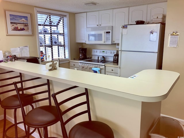 kitchen featuring a breakfast bar area, white appliances, a textured ceiling, white cabinets, and hardwood / wood-style flooring