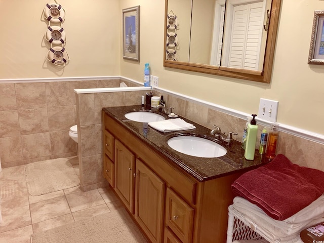 bathroom featuring toilet, tile patterned floors, double sink vanity, and tile walls