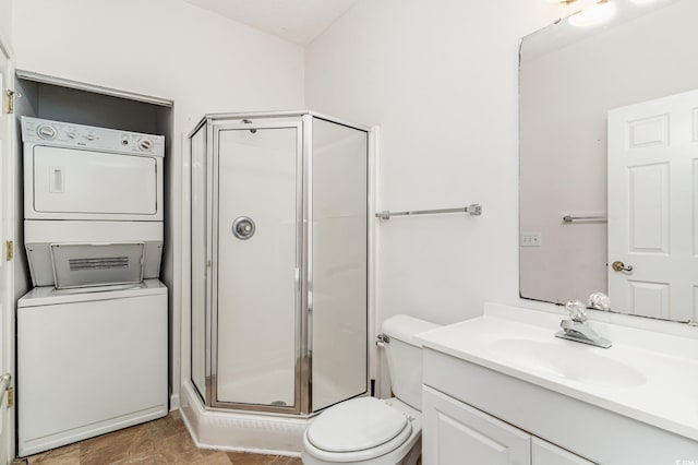 bathroom featuring vanity, stacked washer and dryer, a shower with shower door, and toilet