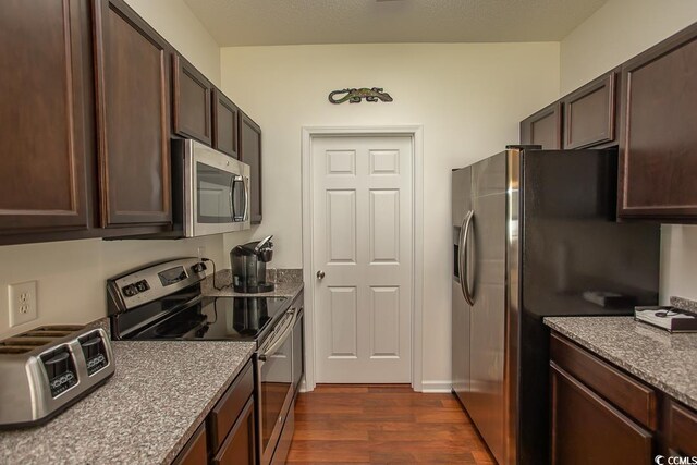 kitchen featuring stone counters, dark brown cabinetry, appliances with stainless steel finishes, and dark hardwood / wood-style floors