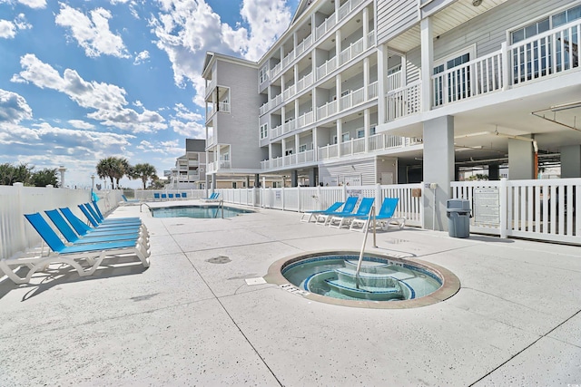 community pool with a patio area, fence, and a community hot tub