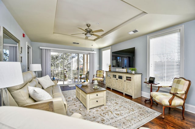 living room with baseboards, visible vents, a raised ceiling, and dark wood-type flooring