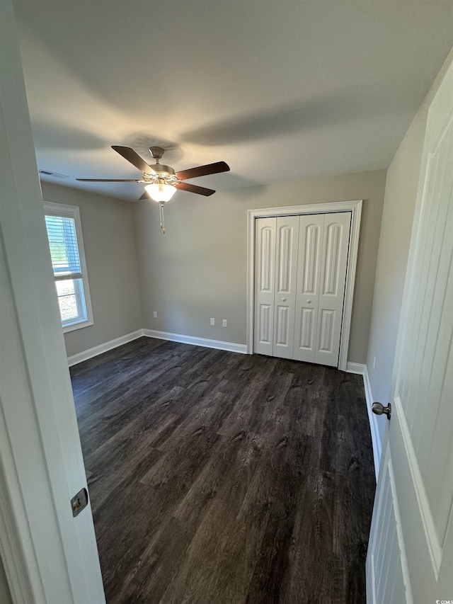 unfurnished bedroom featuring a ceiling fan, baseboards, dark wood-style flooring, and a closet