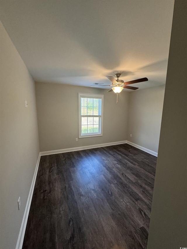 empty room with dark wood finished floors, a ceiling fan, and baseboards