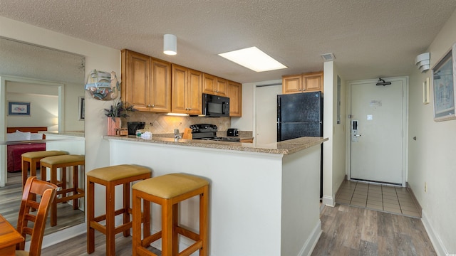 kitchen with black appliances, a kitchen breakfast bar, a textured ceiling, and light tile patterned floors