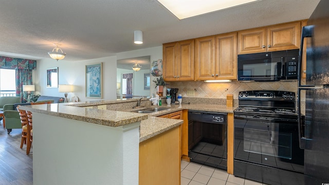 kitchen with backsplash, light stone counters, black appliances, sink, and kitchen peninsula