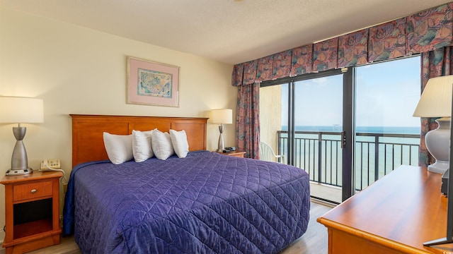 bedroom featuring light wood-type flooring, a textured ceiling, a water view, and access to exterior