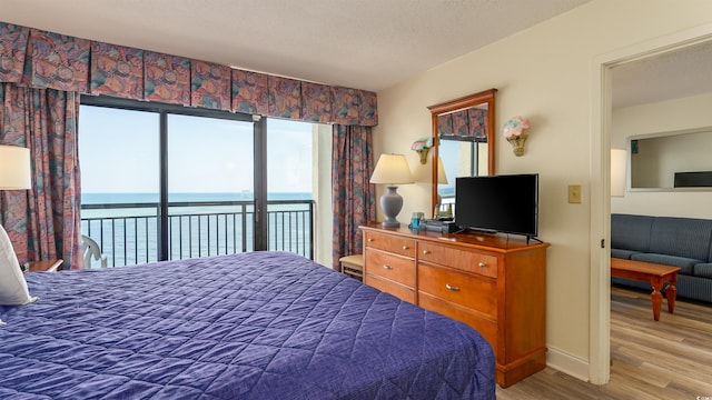 bedroom featuring a textured ceiling, access to outside, a water view, and light hardwood / wood-style floors