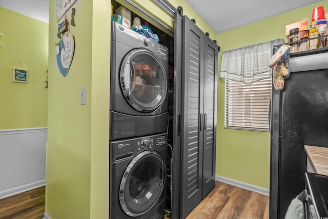 laundry area featuring laundry area, a barn door, stacked washer / dryer, wainscoting, and dark wood-type flooring