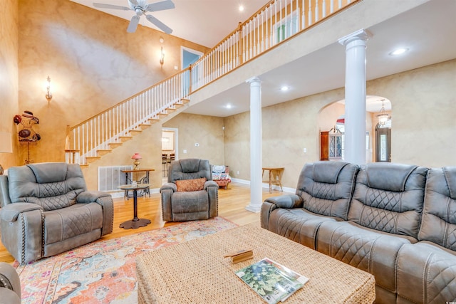 living room featuring ceiling fan, ornate columns, hardwood / wood-style floors, and a high ceiling