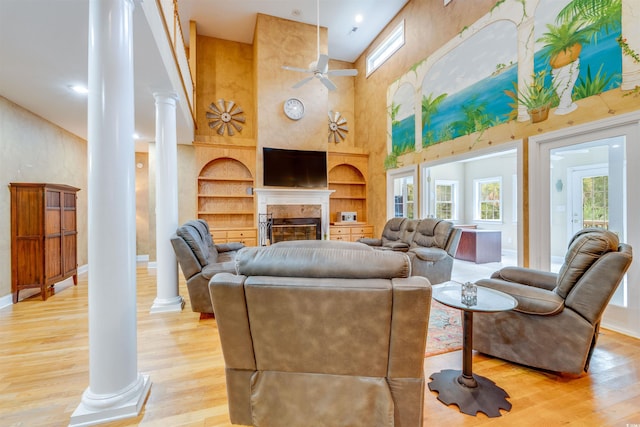 living room featuring ceiling fan, built in features, decorative columns, light wood-type flooring, and a towering ceiling