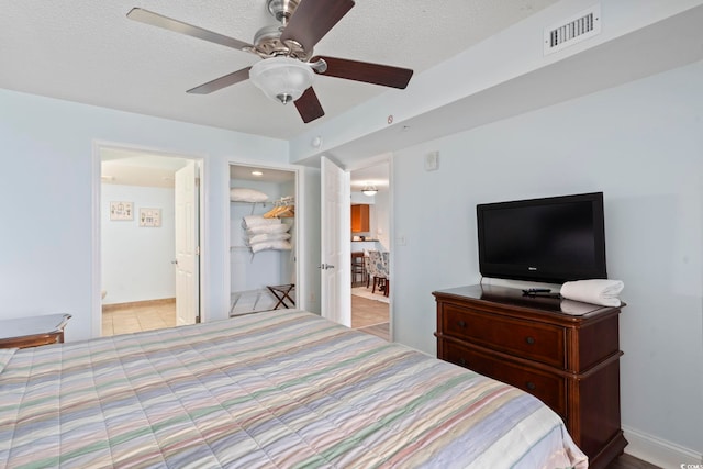 tiled bedroom with ceiling fan, a closet, a textured ceiling, and connected bathroom