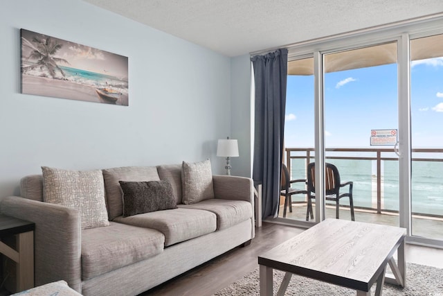 living room featuring a water view, hardwood / wood-style flooring, a textured ceiling, and expansive windows