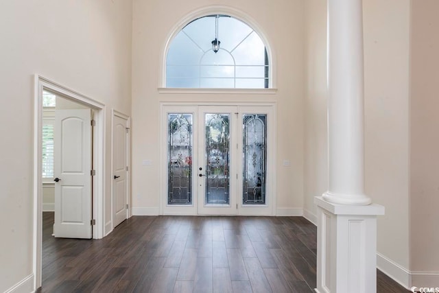 entryway with a towering ceiling, ornate columns, and dark wood-type flooring