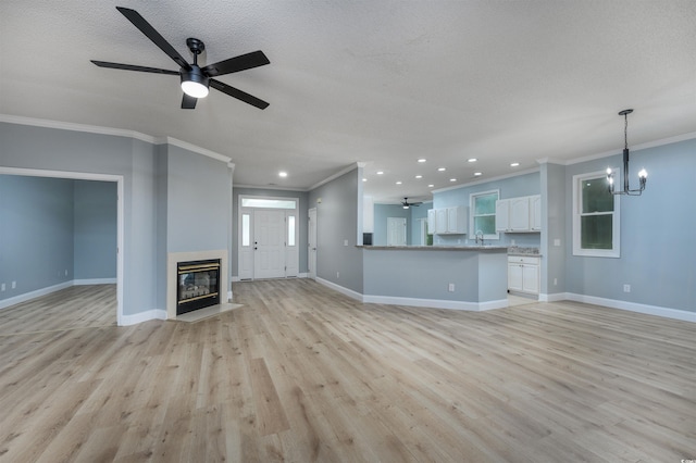 unfurnished living room with ceiling fan with notable chandelier, sink, light hardwood / wood-style flooring, ornamental molding, and a textured ceiling