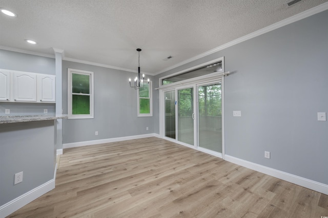 unfurnished dining area with a chandelier, light wood-type flooring, a textured ceiling, and crown molding