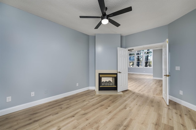 unfurnished living room with ceiling fan, a multi sided fireplace, light wood-type flooring, and a textured ceiling