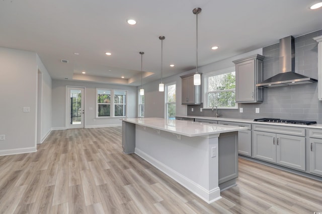 kitchen with light hardwood / wood-style flooring, a kitchen island, hanging light fixtures, and wall chimney range hood