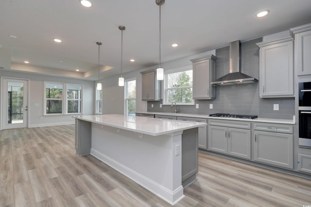 kitchen featuring light wood-type flooring, wall chimney exhaust hood, gray cabinetry, decorative light fixtures, and a kitchen island