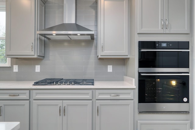 kitchen featuring white cabinetry, wall chimney range hood, appliances with stainless steel finishes, and tasteful backsplash