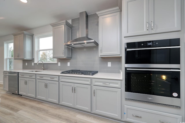 kitchen with backsplash, stainless steel appliances, sink, wall chimney range hood, and light hardwood / wood-style floors