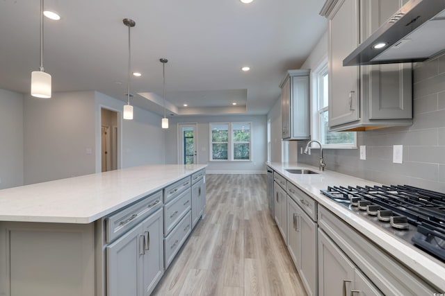 kitchen with hanging light fixtures, a spacious island, extractor fan, light hardwood / wood-style floors, and gray cabinets