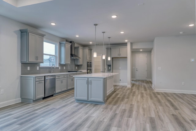 kitchen with wall chimney exhaust hood, stainless steel appliances, light hardwood / wood-style flooring, pendant lighting, and a kitchen island