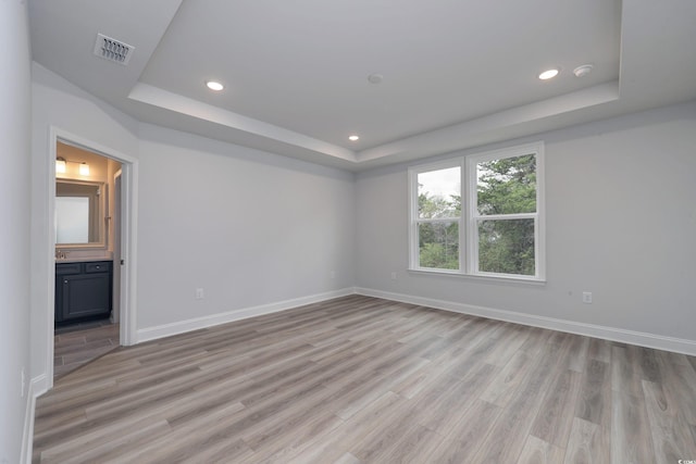 unfurnished room featuring a tray ceiling and light hardwood / wood-style flooring