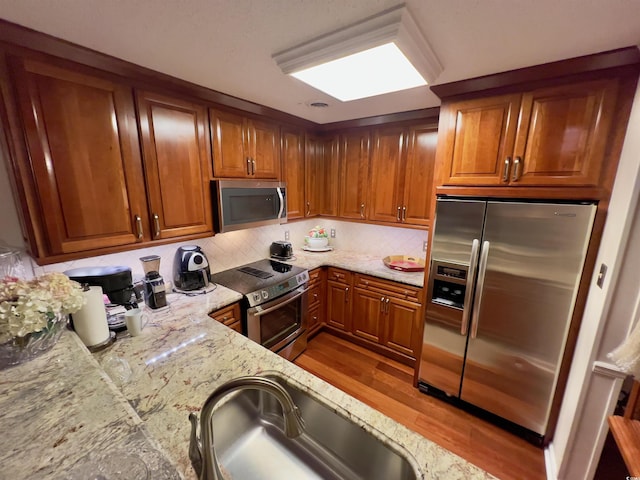 kitchen featuring brown cabinets, light stone counters, stainless steel appliances, and a sink