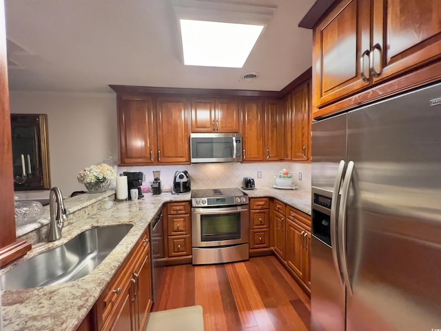 kitchen featuring sink, appliances with stainless steel finishes, light stone countertops, backsplash, and light wood-type flooring